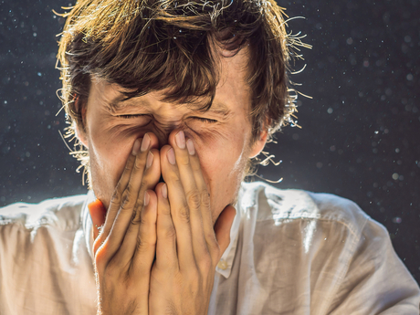 man sneezing into hands