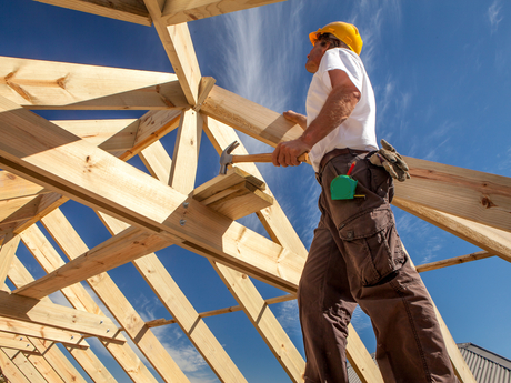 Builder working on framing of home during blue, sunny day