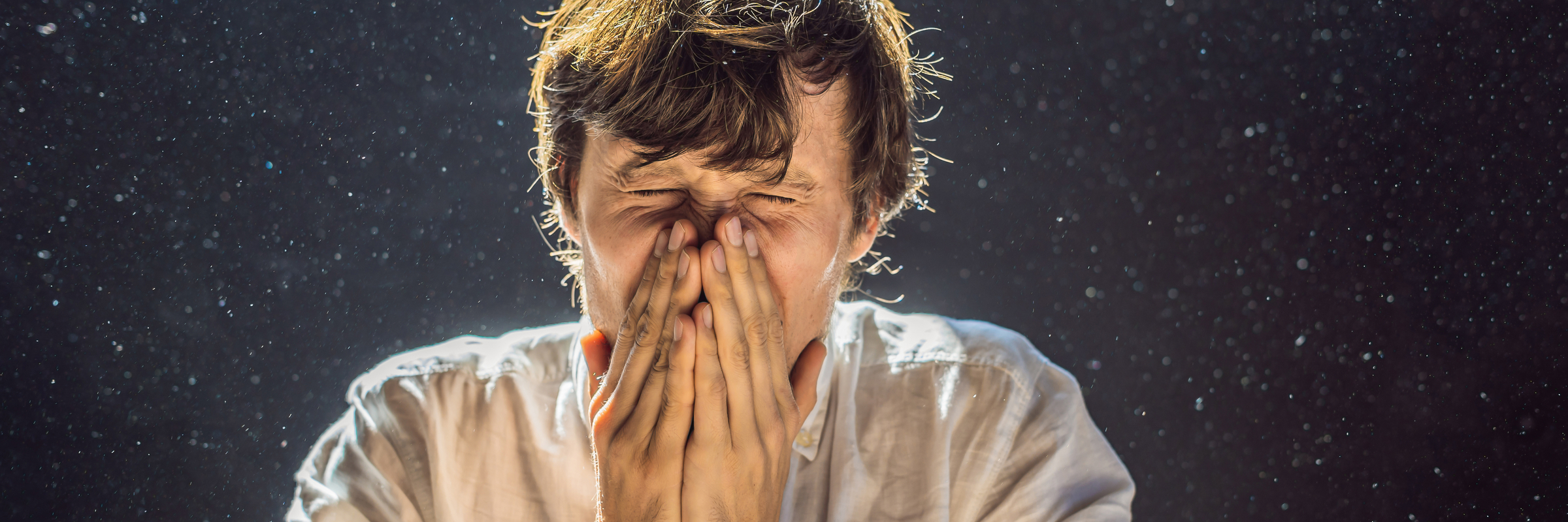 man sneezing into hands